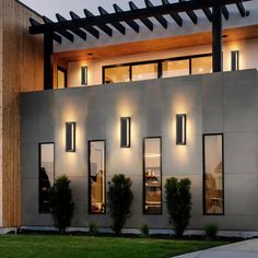 an exterior view of a modern house with lights on the windows and grass in front