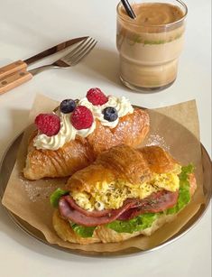 two croissants with meat, cheese and berries on them next to a cup of coffee