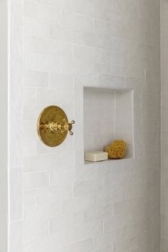 a bathroom with white tile and gold fixtures on the shower wall, along with yellow sponges