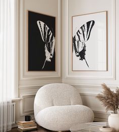 a white chair sitting in front of two paintings on the wall next to a coffee table