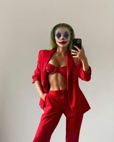 a woman dressed as the joker taking a selfie with her cell phone while standing in front of a white wall