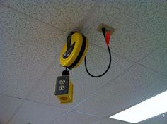 a yellow and black alarm clock hanging from the ceiling in an office building with two wires attached to it