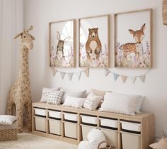 a nursery room with three pictures on the wall and two stuffed giraffes