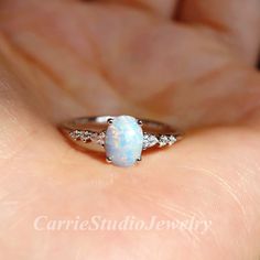 a close up of a person's hand holding a ring with a white opal