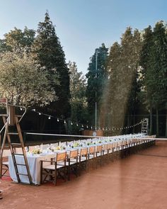 a long table is set up with white linens and place settings for an outdoor dinner