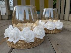 two clear glass vases with white flowers on them sitting on a wooden table outside