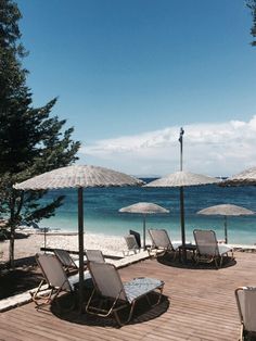 lounge chairs and umbrellas on a wooden deck next to the ocean with clear blue water