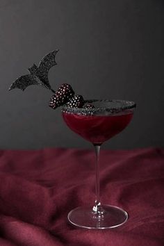 a halloween drink garnished with blackberries and sprinkles on a red cloth