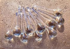 a bunch of glass spoons sitting on top of a dirt floor next to each other