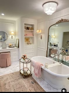 a white bath tub sitting in a bathroom next to a large mirror and table with flowers on it