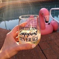 someone holding up a wine glass in front of a pink flamingo floater that says,'emotion support beverage '