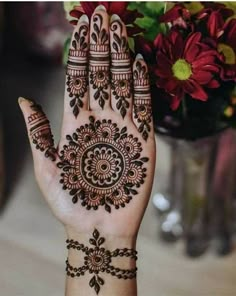 a woman's hand with henna tattoos on it and flowers in the background