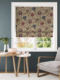 a chair and table in front of a window with a flowered roman blind on it