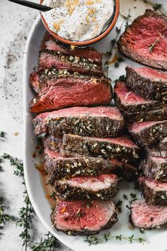 sliced steak on a white platter with a small bowl of ranch dressing