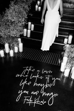 a woman in a white dress is walking down the stairs with candles and flowers around her