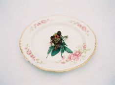 a plate with flowers on it sitting on a white tableclothed surface, in the center is a gold rim