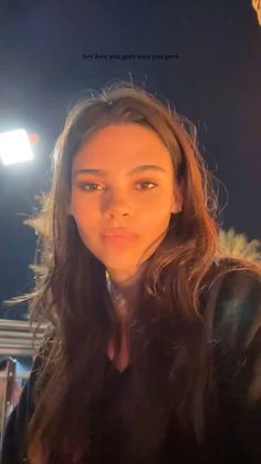 a woman with long brown hair standing in front of a camera and looking at the camera