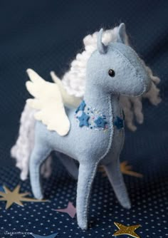 a blue stuffed horse with white wings and flowers on it's tail, standing in front of stars