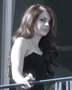 a woman in a black dress standing on a balcony with her hand on the railing