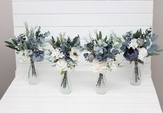 three vases with flowers and greenery are lined up against a white board wall