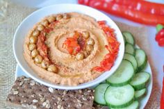 hummus, crackers and cucumbers on a plate with red chili peppers