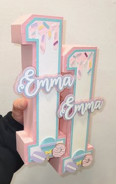 a person holding up a pink and white letter shaped like an ice cream shop sign