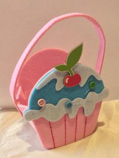 a pink cupcake with a cherry on top is sitting next to a small basket