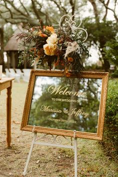 a welcome sign with flowers and greenery in front of a wooden easel on the grass