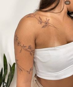 a woman with a tattoo on her arm and shoulder is standing in front of a potted plant