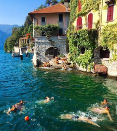 people swimming in the water next to buildings and trees on both sides of the lake