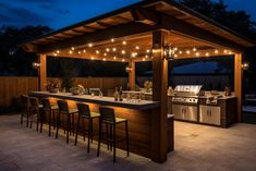 an outdoor kitchen and bar with lights strung over it at night, lit up by string lights