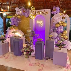 a stage set up for a party with purple and gold decorations on the walls, candles and balloons