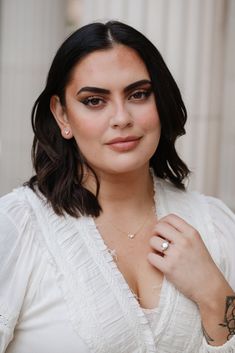 a woman wearing a white shirt and holding a ring on her finger, looking at the camera