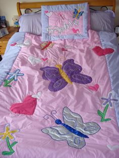 a child's bed with pink and purple comforter, butterflies and hearts on it