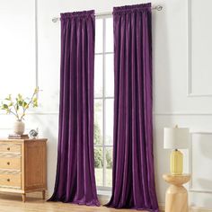 a living room with purple curtains and a wooden table in front of the window that has a vase on it