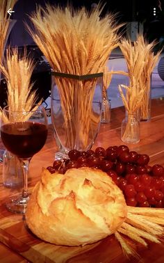 bread, grapes and wheat on a wooden table with wine glasses in the foreground