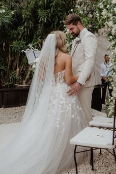 a bride and groom standing in front of an arch with white flowers on it at their wedding ceremony