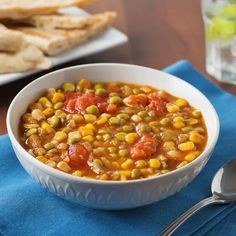 a bowl of corn and tomato soup on a blue napkin next to some pita bread