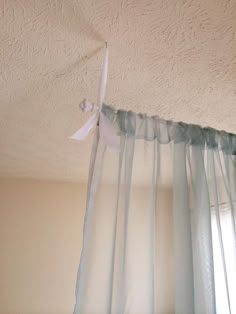 the curtains are hanging from the ceiling in front of the window with white ribbons on them