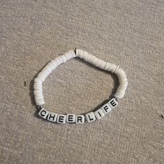 the word cheer life spelled with letters on a white beaded bracelet laying on carpet