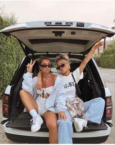 two women sitting in the back of a car with their arms up and one holding her hand up