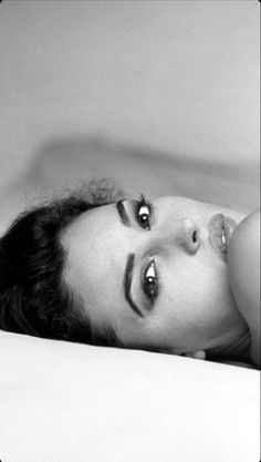 a black and white photo of a woman laying on a bed looking at the camera