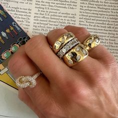 a person's hand with three rings on top of their fingers and an open book in the background