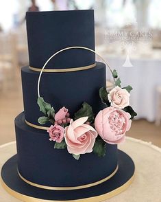 a three tiered blue wedding cake with pink flowers on the top and gold trim