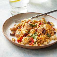 a white plate topped with pasta and meat next to a glass of water on a table