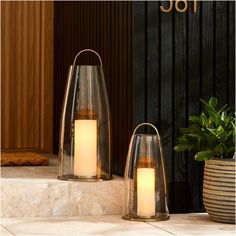 two clear glass candle holders sitting on steps next to a potted plant and door