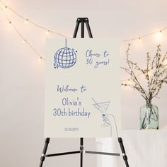 a white sign sitting on top of a easel next to a vase filled with flowers