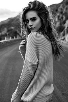 a black and white photo of a woman with long hair wearing a sweater on the street