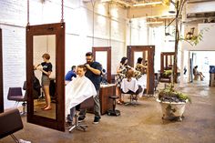 a group of people getting their haircuts in a room with mirrors and chairs