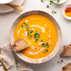 a bowl of carrot soup with bread on the side